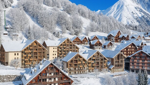 Un complejo turístico en la montaña cubierto de nieve, con chalés de madera y un telesilla.