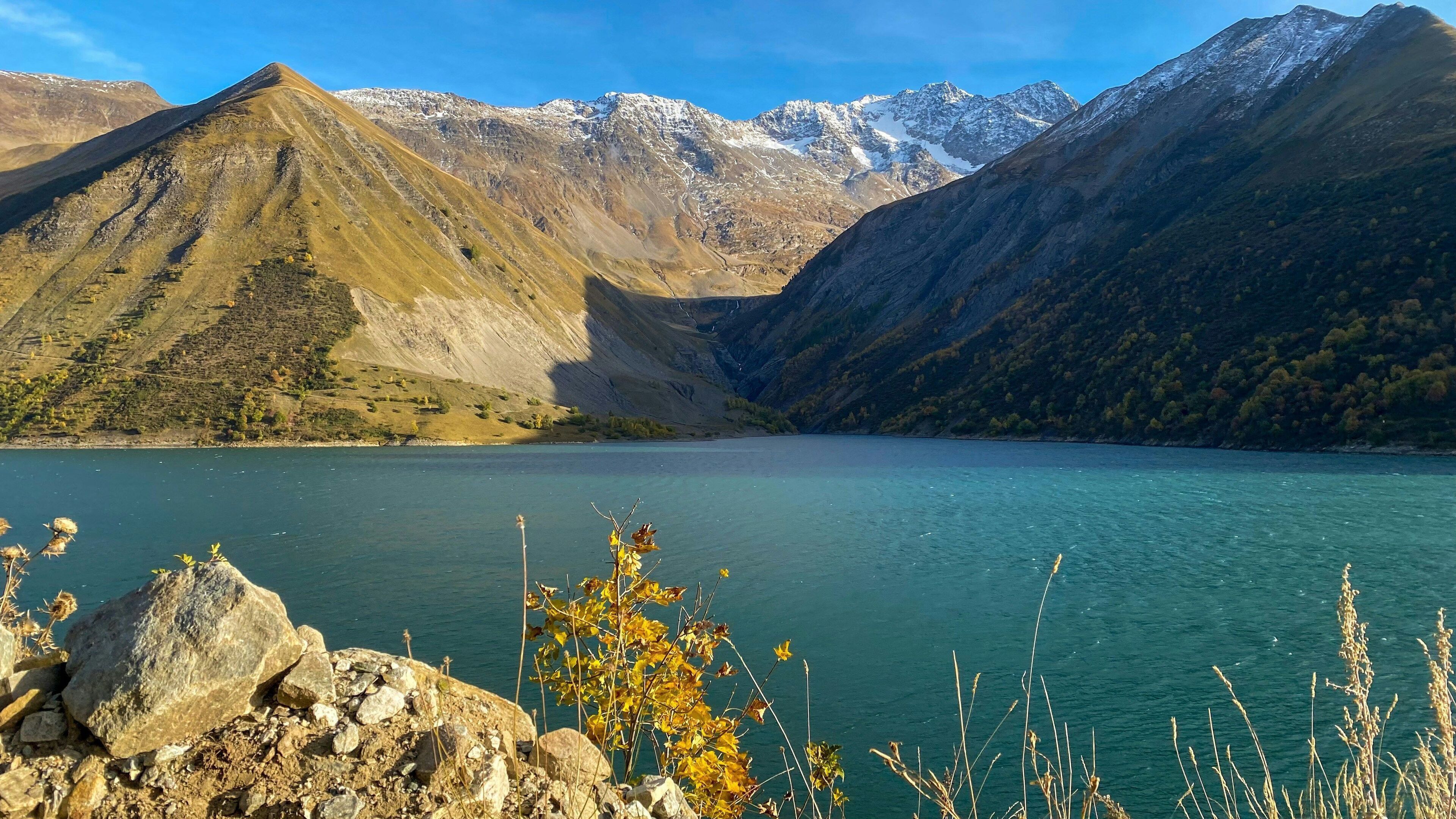 Un paisaje montañoso con un lago, un primer plano rocoso y picos nevados.