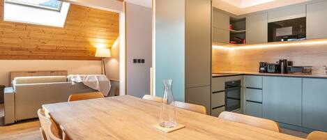 A modern kitchen with built-in appliances, a dining area with a wooden table and chairs, and a cozy seating area with a sofa and lamp.