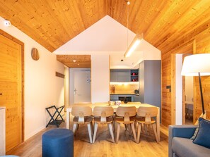 A modern interior with a wooden ceiling, a central dining table with chairs, a sofa, and a lamp.