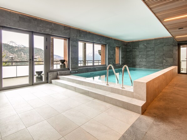 Una piscina interior con vistas a montañas, paredes de piedra y techo de madera.