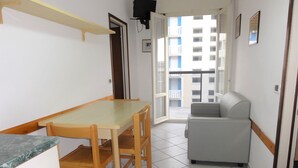 A small, bright room with a wooden table and chairs, a grey sofa, and a view of a building through an open door. - Sea View Flat Near Piazzale Zenith (San Michele al Tagliamento)