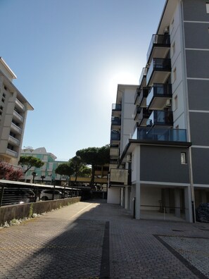 A paved pathway between two modern apartment buildings with balconies, a clear sky, and a parked car. - Relaxing sea View Stay Near the Promenade (San Michele al Tagliamento)