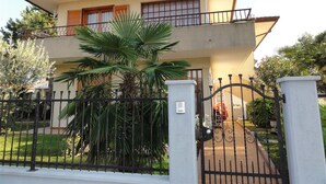 A two-story house with a balcony, a gated entrance, and a large palm tree in the front yard.