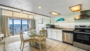 A modern kitchen with a large island, a dining area with a glass table, and a view of the water through large windows. - Top Floor 🪸 Private Balcony 🪸 View of the Gulf (Cedar Key)