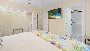 A bedroom with a bed, a ceiling fan, a door leading to a bathroom, and a painting on the wall. - Cedar Key Seaside Escape (Cedar Key)