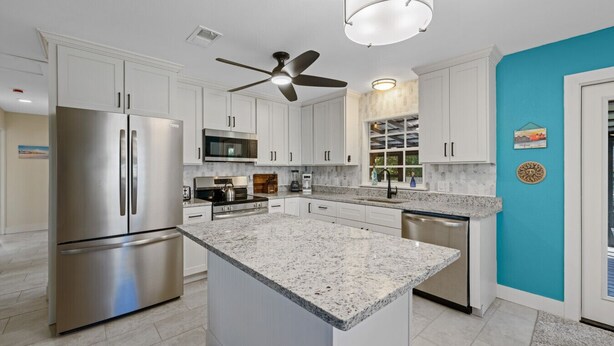 A modern kitchen with white cabinetry, stainless steel appliances, and a granite countertop. - Cedar Key Seaside Escape (Cedar Key)