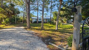 A gravel driveway leading to a house with a blue roof, surrounded by trees and a grassy lawn. - Cedar Key Seaside Escape (Cedar Key)