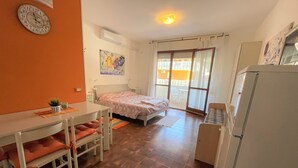 A compact bedroom with a bed, a small table with chairs, a refrigerator, and a window with curtains.