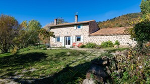A stone house with a tiled roof, a front door, and a small garden with flowers and a pathway. - Le Mas Victor Ardèche – Tranquility and Nature Near Saint-Victor (saint victor)