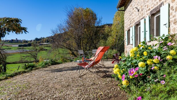 A stone building with a gravel driveway, a red folding chair, and a garden with yellow and pink flowers. - Le Mas Victor Ardèche – Tranquility and Nature Near Saint-Victor (saint victor)