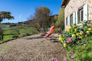 A stone building with a gravel driveway, a red folding chair, and a garden with yellow and pink flowers.