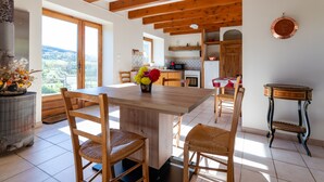 A spacious kitchen with wooden beams, a dining area with a large table and chairs, and a view through the window. - Le Mas Victor Ardèche – Tranquility and Nature Near Saint-Victor (saint victor)