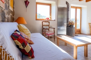 A bedroom with a bed, a chair, a table, a window, and a fireplace.