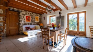 A cozy room with a wooden ceiling, stone walls, a bed with colorful pillows, a dining table with chairs, and a large window with a view of greenery. - Le Mas Victor Ardèche – Tranquility and Nature Near Saint-Victor (saint victor)