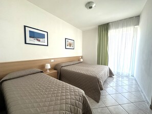 Une chambre d’hôtel avec deux lits, une tête de lit, une table de chevet avec une lampe et deux tableaux encadrés au mur.