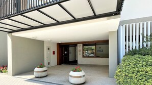 A building entrance with a covered walkway, two planters with flowers, and a green hedge. - Bibione Flat With Side sea View (San Michele al Tagliamento)