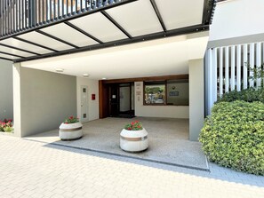 A building entrance with a covered walkway, a door, and two planters with flowers. - Bibione Flat With Side sea View (San Michele al Tagliamento)