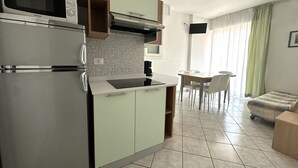 A compact kitchen with a microwave, stove, and sink. There is a dining area with a table and chairs. - Bibione Flat With Side sea View (San Michele al Tagliamento)