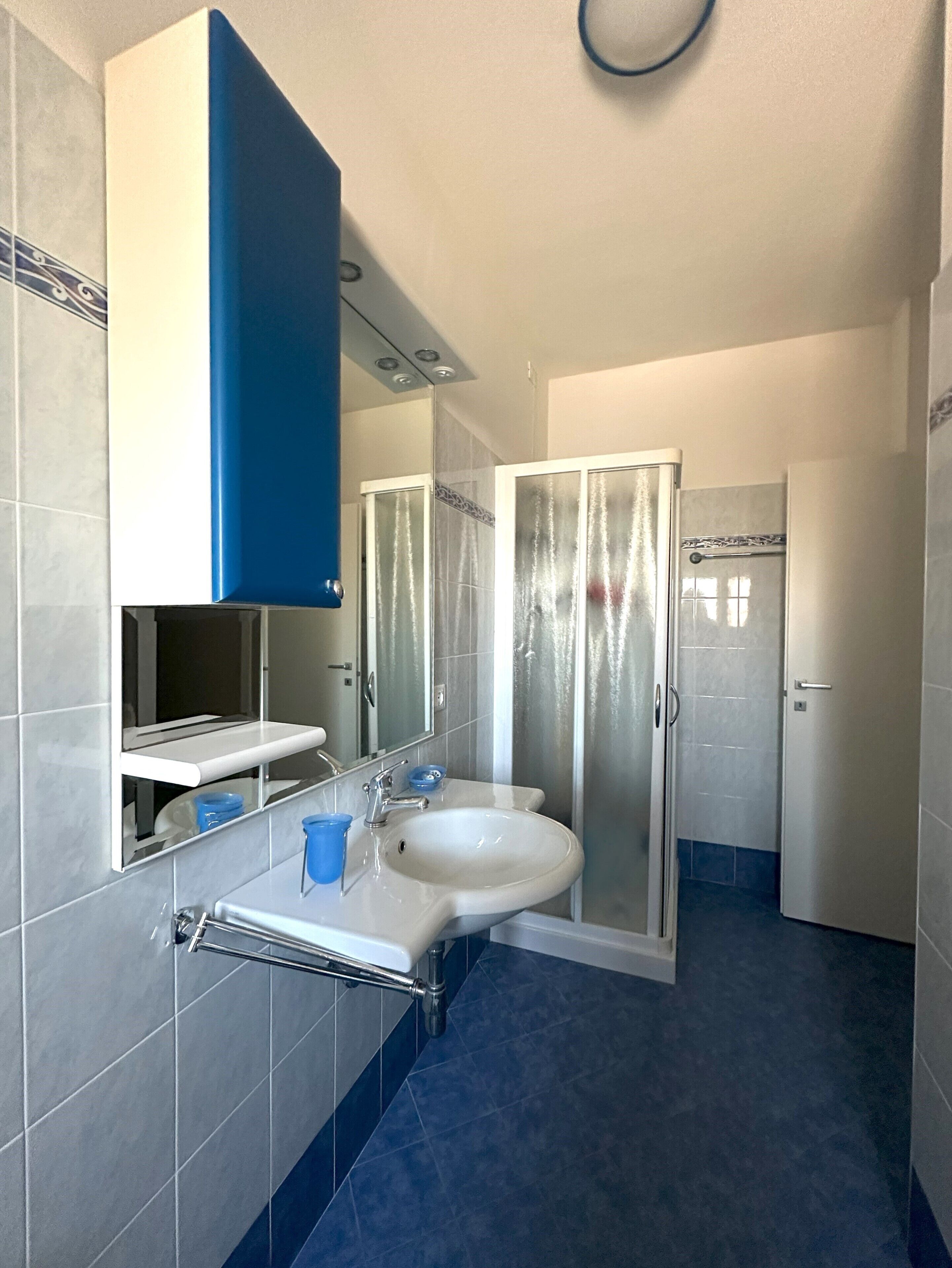 A bathroom with a white sink, blue tiles, a glass shower enclosure, and a mirror above the sink.