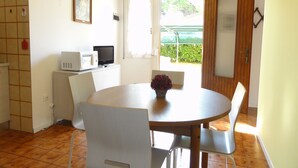 A room with a round table, white chairs, a small TV, and a window with a view of greenery.