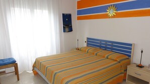 A bedroom with a bed, a nightstand, a chair, and a wall with a painting. - Modern Apartment With Terrace (San Michele al Tagliamento)