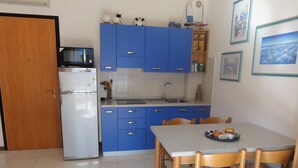 A compact kitchen with blue cabinets, a white refrigerator, a microwave, and a dining area with wooden chairs and a table. - Modern Apartment With Terrace (San Michele al Tagliamento)