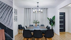 A modern dining room with a long table, black chairs, a chandelier, and a large plant. - VillaVerde 4BRs/Pool/Sleeps16/Gym/Gameroom/HTX/NRG (Houston)
