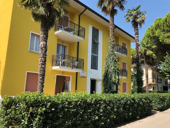 Un bâtiment jaune doté de balcons, une enseigne indiquant « Villa Palma », et une végétation luxuriante tout autour.