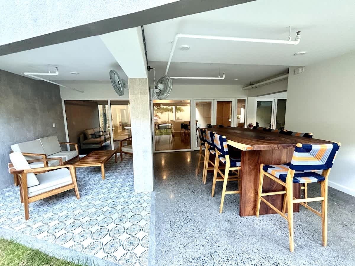 A spacious outdoor dining area with a wooden table and chairs, a sofa, and a patterned floor.