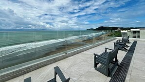 A rooftop terrace with a glass balustrade overlooking the sea, featuring outdoor seating and a clear view of the coastline. - Stunning Beachfront 1BR Suite with Ocean View (Jacó)