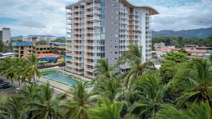 A multi-story hotel with balconies, a swimming pool, and a view of surrounding buildings and palm trees. - Stunning Beachfront 1BR Suite with Ocean View (Jacó)