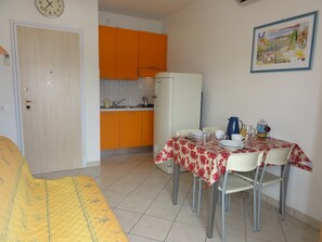 A compact living space with a dining area, kitchen, and a bed. - Cozy Apartment by the Beach (San Michele al Tagliamento)