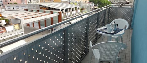 Ένα μπαλκόνι με δύο λευκές καρέκλες και ένα τραπέζι, με θέα την πόλη, τα κτίρια και ένα τρένο.