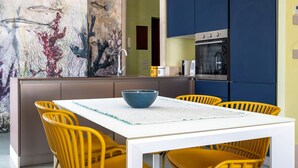 Eine moderne Küche mit einem weißen Tisch und gelben Stühlen, einer großen Fischwandmalerei und einem eingebauten Backofen.