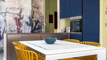 Une cuisine moderne avec une table blanche et des chaises jaunes, une grande fresque représentant des poissons et un four encastré.