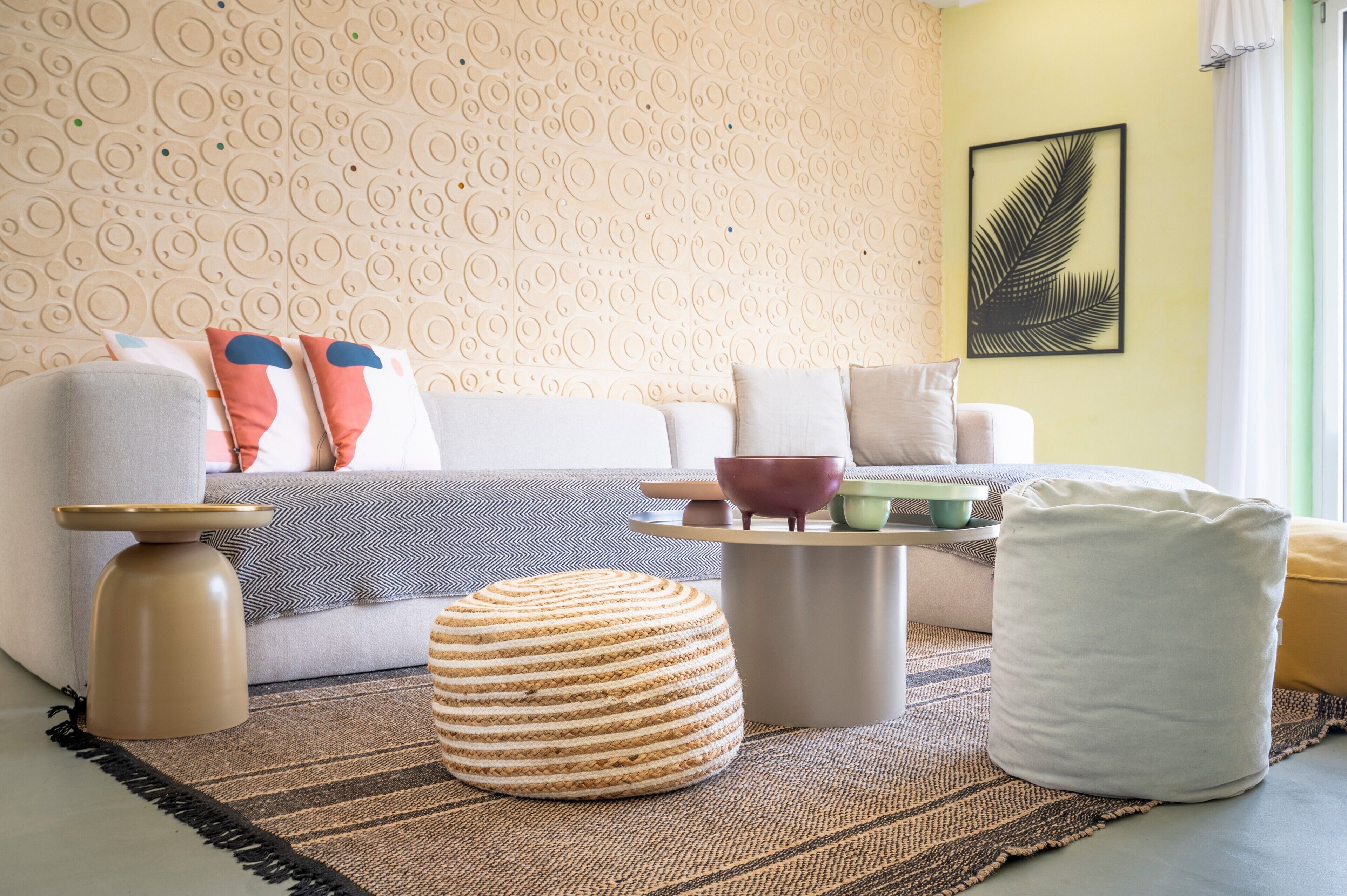Un salon comprenant un canapé, un pouf, une table basse et des éléments de décoration murale.