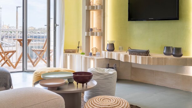 Ein modernes Wohnzimmer mit Fernseher, Regalen mit Dekoration, einer Essecke mit Tisch und Stühlen sowie einem Blick durch große Fenster.