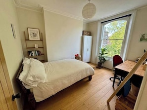 A bedroom with a bed, a desk, a chair, a radiator, and a window.
