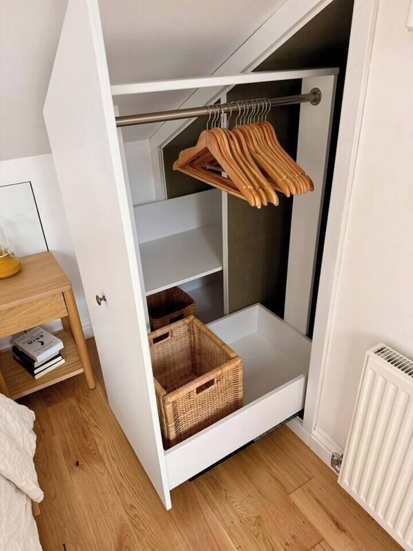 A white wardrobe with shelves and hanging space, a wooden hanger, and wicker baskets.