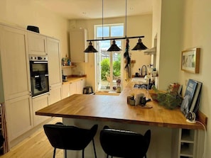 A kitchen with a wooden island, black chairs, pendant lights, and a view to the outside.
