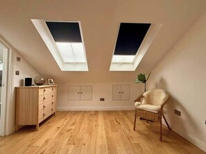A room with a wooden floor, a wooden dresser, a wicker chair, and two skylights.