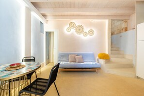 A modern interior with a round table, black chairs, a sofa with cushions, a wall with decorative patterns, and a staircase.