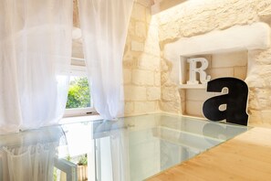A room with a glass table, white curtains, a stone wall, and letters 'R' and 'a' on shelves.