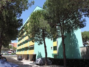 A multi-story building with a green and yellow facade, surrounded by trees. - Condominium Flat Near Bibione Spiaggia (San Michele al Tagliamento)