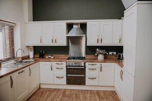 A modern kitchen with white cabinets, a stainless steel range hood, and a wooden countertop. - Cobbled Curlew, Patty's Barn , Lancaster 4* (Lancaster)