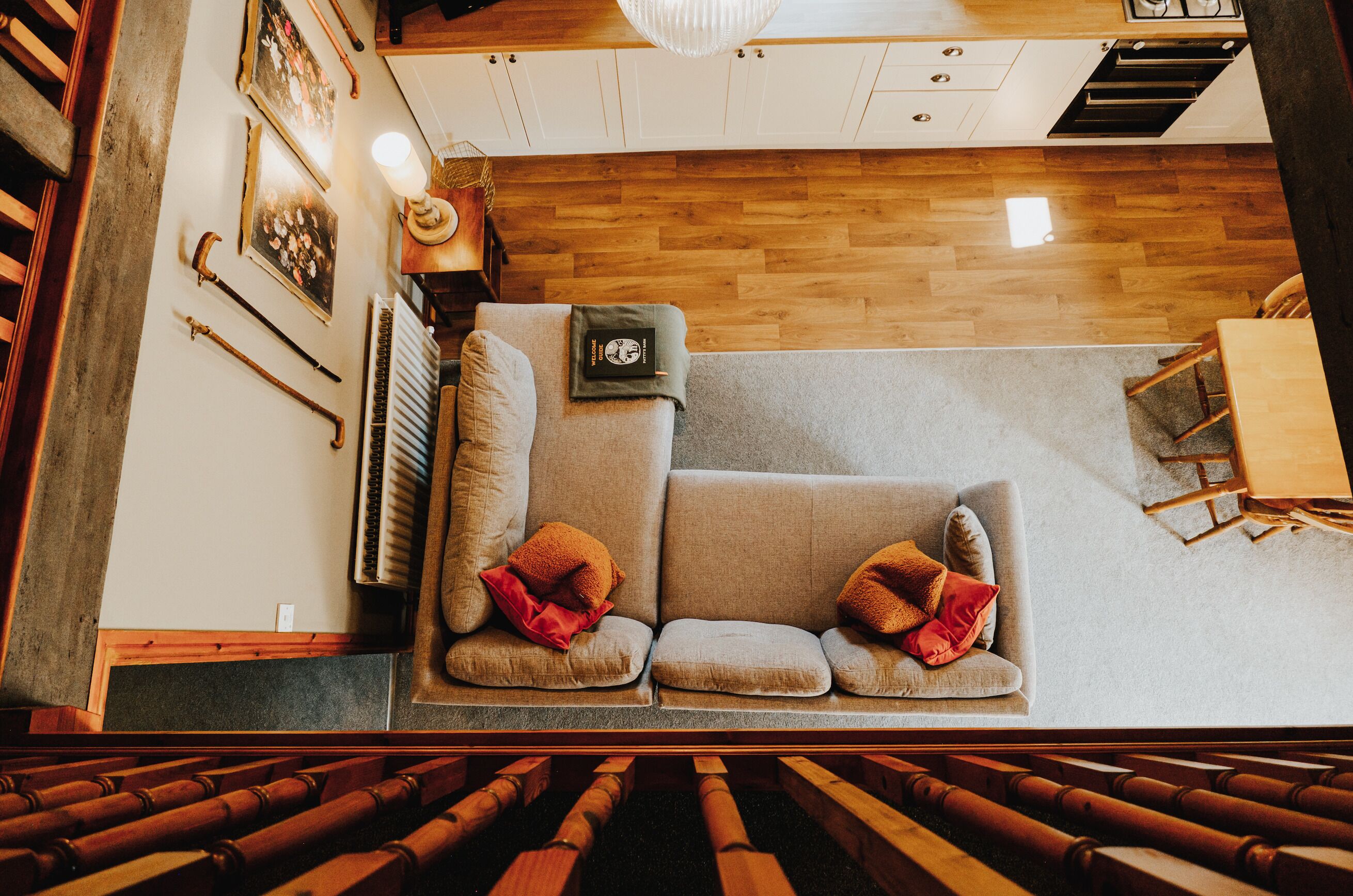 A room with a wooden floor, a grey sofa with cushions, a small table, and a radiator.