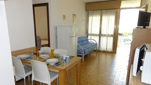 A compact room with a dining table, chairs, a bed, a TV, and a refrigerator.