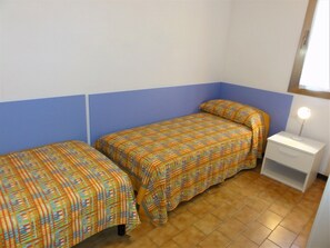 Eine kleine, einfache Unterkunft mit zwei Einzelbetten, einem Nachttisch und einem fenster mit Vorhängen.