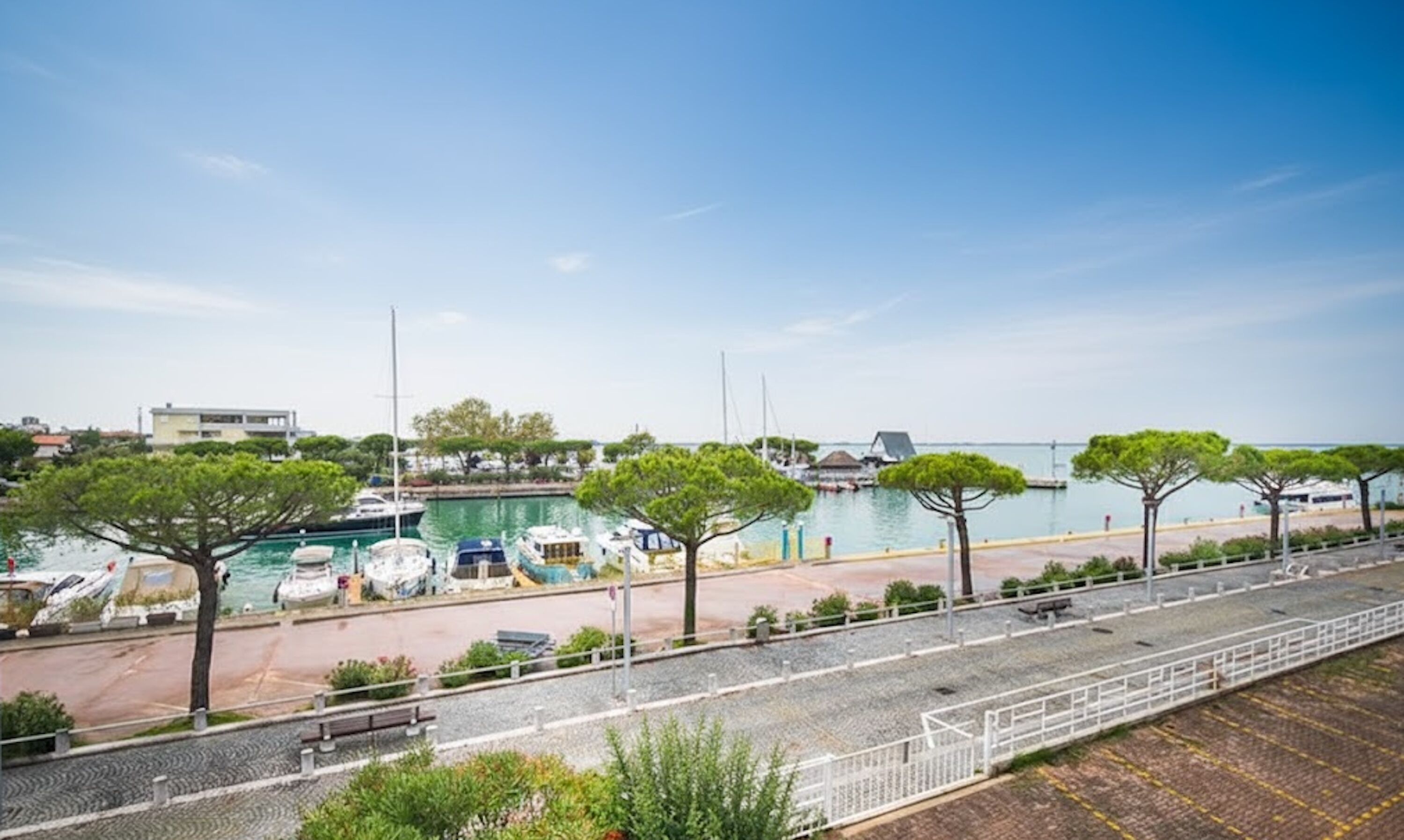 A marina with boats docked, a pedestrian path, and trees lining the waterfront.